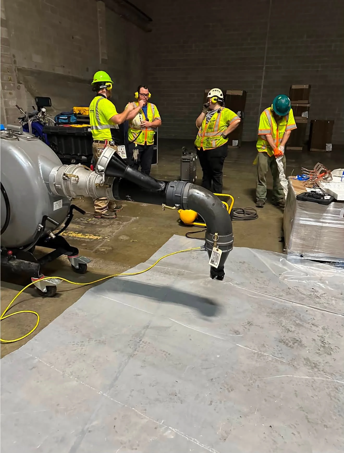 Workers beside pipe-lining installation equipment inside a building.