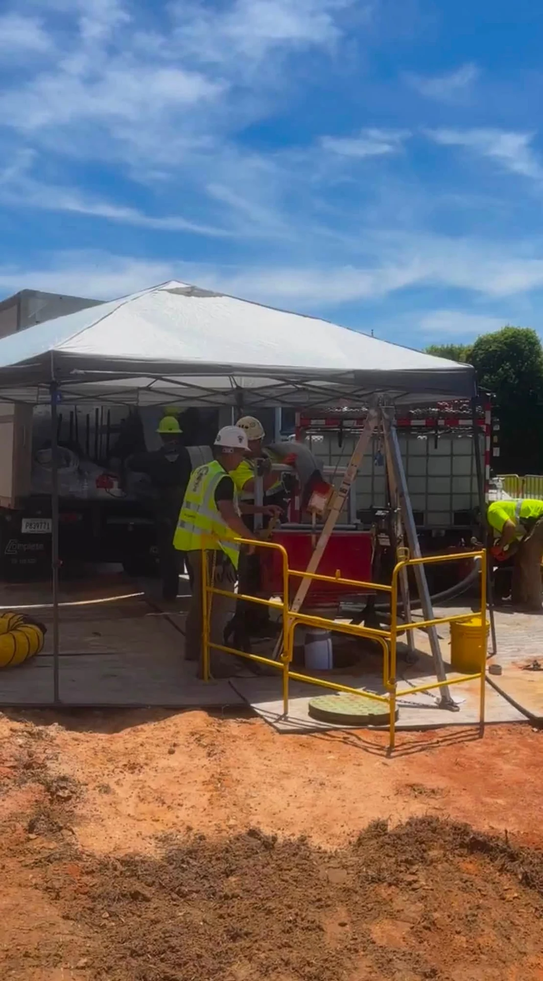 Workers beside a guarded pipe access opening and canopy.